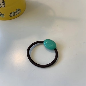 Detail view of a black high-elastic hair tie with a smooth green oval bead accent