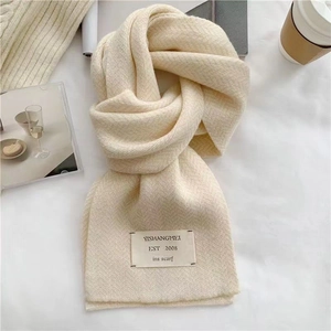 Détail de l'écharpe en tricot beige montrant la texture et l'étiquette de la marque