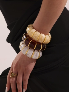 Macro shot of 18k gold resin bracelets and green gemstone ring on model wrist