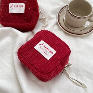 Detail of red corduroy coin purse with zip closure and decorative ribbon on soft white cloth