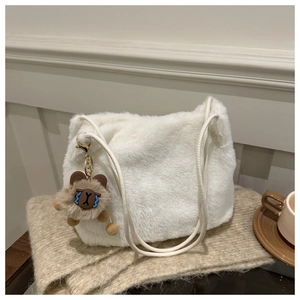 Detail of soft white plush shoulder bag featuring a cute brown bear charm for winter fashion