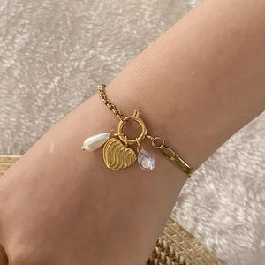 Dettaglio di un bracciale a catena snake dorata con ciondoli a cuore, perla e cristallo