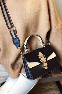 Close-up of contrast crossbody bag with golden horseshoe buckle and wide striped strap