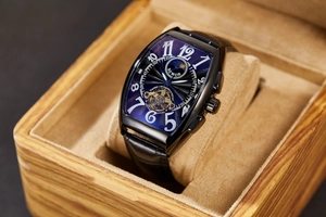 Macro detail of tonneau mechanical watch with blue dial and leather strap in wood box