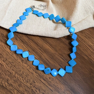 Detailed shot of blue diamond-shaped beaded necklace with silver lobster clasp on wood