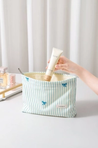 Detail of hand putting skincare into a striped fabric pouch with bow embroidery