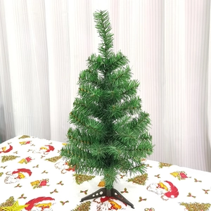 Detailed view of a 30cm mini green artificial Christmas tree with a black base on a festive cloth