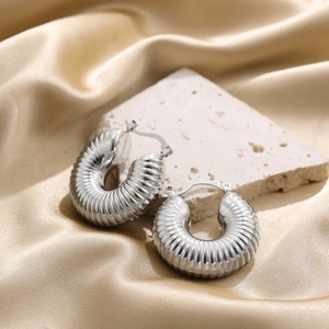 Detailed macro shot of silver hollow textured hoop earrings on a marble stone surface