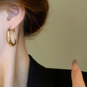 Close-up of minimalist chunky gold hoop earrings with polished finish worn by a model