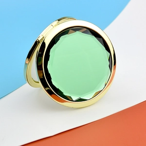 Detail of round golden folding mirror with a large faceted green gemstone inlay