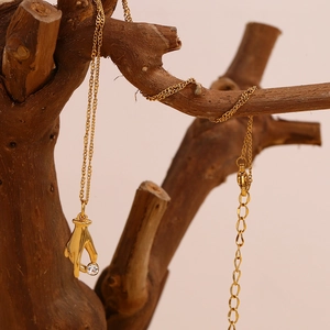 Detail of 18K gold hand-shaped pendant holding a clear diamond on a rustic wooden branch