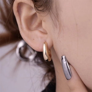 Close-up of a polished gold geometric C-shaped earring showing mirror-like finish on model