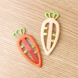 Detail view of two carrot-shaped hair clips in orange and beige on a wooden surface