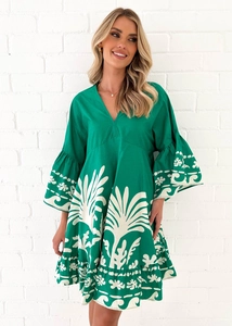 Detailaufnahme des V-Ausschnitts und weißen Blumendrucks auf dem grünen Kleid