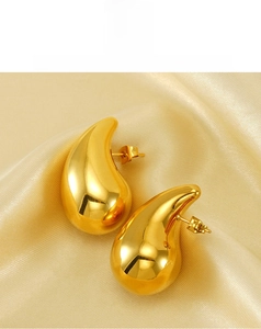 Detailed view of polished 18K gold plated teardrop earrings on soft silk fabric background