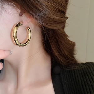 Close-up profile of a model wearing smooth golden C-shaped metal hoop earrings