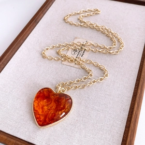 Detail of amber heart pendant with golden chain on vintage textured background