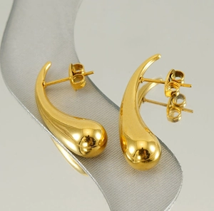 Detail of polished gold drop earrings with a sleek mirror finish on a reflective surface