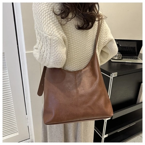Close-up of a brown leather tote bag with natural texture shown on a female model