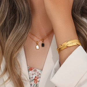 Golden necklace with black and white pendants and feather-shaped bracelet on model