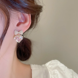 Macro detail of gold-plated bow pearl earring with a heart-shaped pink zircon stone