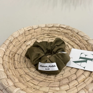Close-up of olive green textured fabric scrunchie with brand label on straw tray