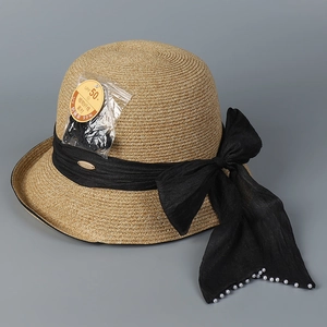 Detail of beige straw hat featuring black satin bow with pearl accents and UPF 50+ tag