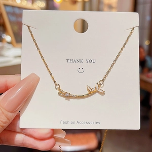 Close-up of golden fishtail pendant necklace with sparkling white zircons on display card