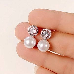 Close-up of elegant pearl earrings with pavé zircons held to show scale and detail