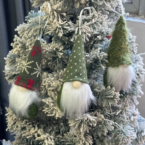 Close-up of knit Christmas gnomes with snowflake patterns hanging on snowy tree branches