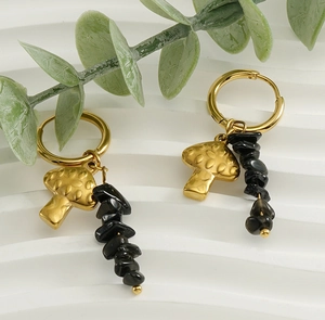 Detail of gold mushroom earrings with natural black stones on white textured background
