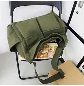 Detail of army green canvas messenger bag with double pockets and flap design on a chair
