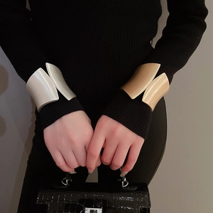 Close-up of matte gold and silver wide irregular cuff bracelets on black knitwear