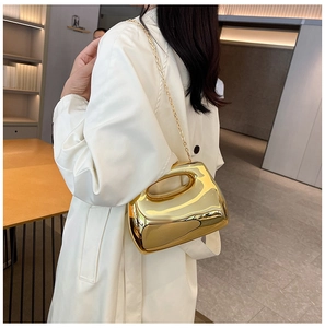 Mirror gold acrylic evening clutch bag worn over a long white coat in an indoor setting