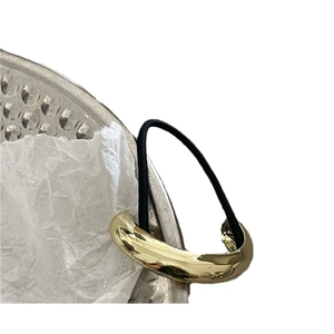 Minimalist gold mirror alloy ponytail cuff with black elastic band on metal tray