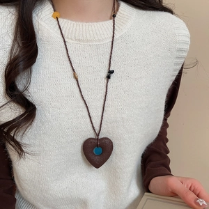 Close-up of a vintage heart pendant necklace with blue bead detail on a knit vest