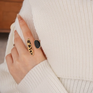 Close-up of golden geometric ring with leopard print and black enamel on knit fabric