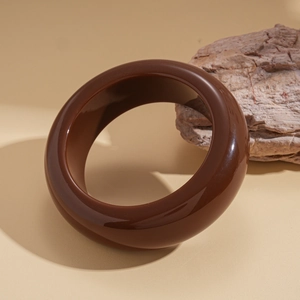 Macro detail of glossy dark brown resin geometric bangle resting against natural rock