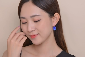 Close-up of elegant blue oval gemstone drop earrings worn by a model in soft studio light