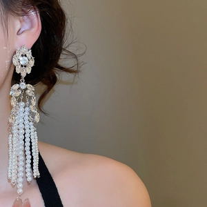 Close-up of luxury flower earrings with white pearl tassels worn by a model