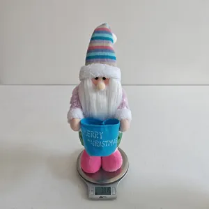 Plush Christmas gnome with colorful striped hat holding a Merry Christmas bucket for decor