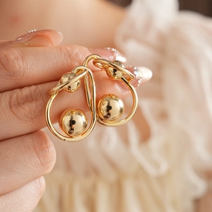 Close-up of golden twisted ball earrings with fluid design worn on model ear