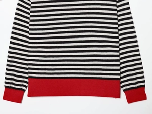 Detail of black and white striped knit sweater featuring contrasting red ribbed cuffs