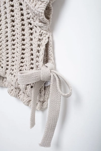 Détail macro d'un pull en maille beige avec nœuds latéraux et motif de tricot ajouré