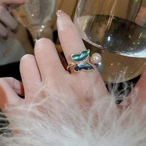 Detail of gold butterfly ring with pearl and abalone shell worn on woman's finger