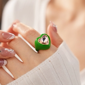 Detail of green enamel heart ring with a pink crystal gemstone on a model's finger