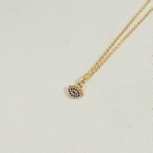 Close-up of golden necklace with evil eye pendant featuring blue and clear zircon stones