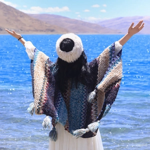 Ethnic knit shawl with blue and brown patterns and tassels shown at a scenic lake view