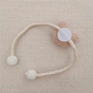 Detail of beige plush bear curtain tieback with woven rope and white pearl bead accents
