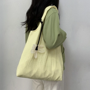 Detail of cream pleated canvas tote bag with floral charm worn over the shoulder